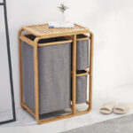 Panier à linge en bambou et tissu gris dans une salle de bain avec une petite plante verte posée dessus.