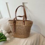 Photo d'un panier de plage tissé en rotin posé sur une table avec une nappe beige et des fleurs.