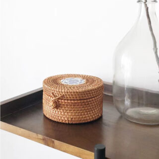 Photo d'un panier de rangement en rotin avec couvercles fermé par un bouton, posé sur une table en bois avec un vase transparent.