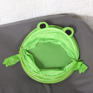 panier pour enfants pliable en tissu, en forme de grenouille verte, plié sur une surface en tissu gris