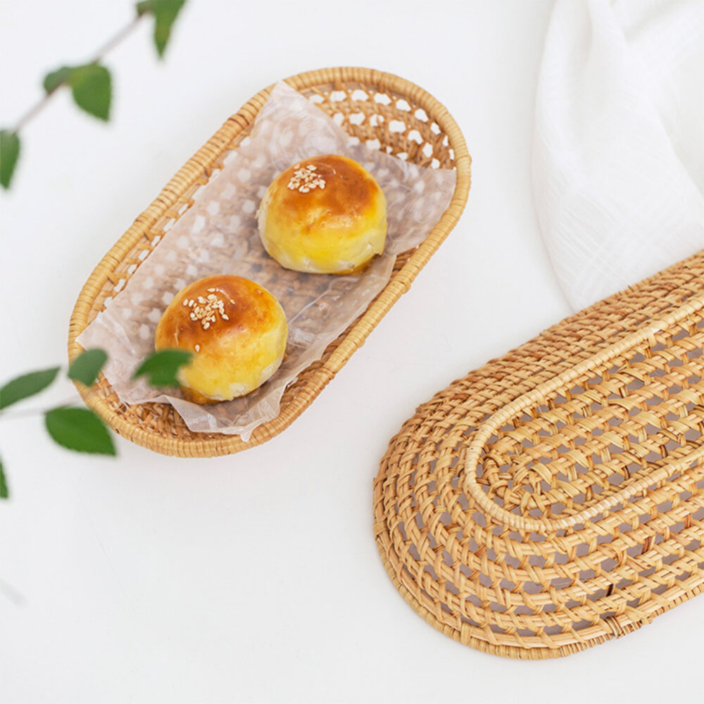 Panier à pain ovale en rotin avec des petits pains dedans posés sur une table avec une nappe blanche