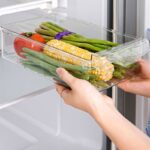 Personne tenant un panier coulissant pour le frigo, rempli d'aliments.