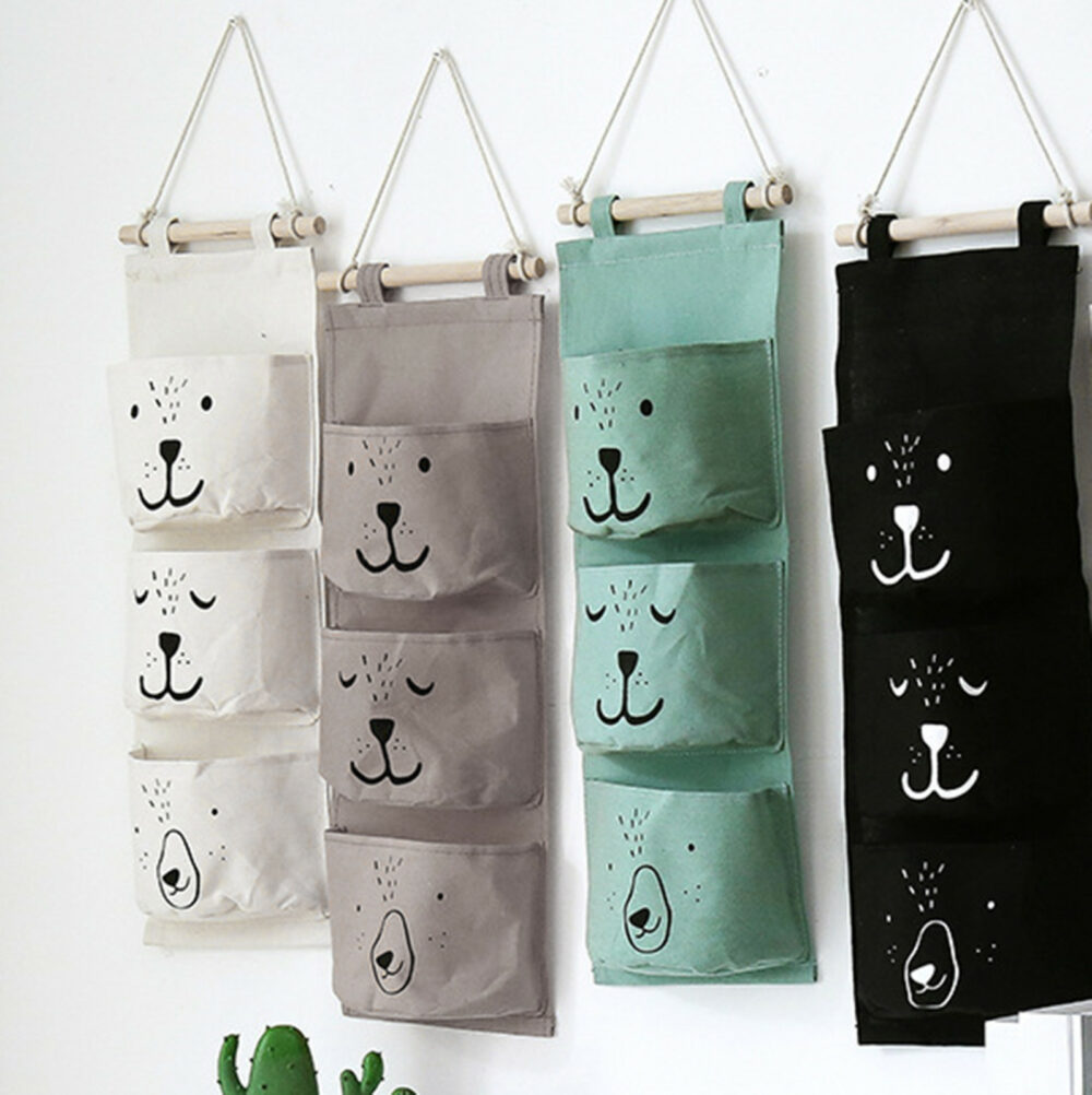 3478-81wnr6.jpg quatre paniers de rangement pour enfants à trois poches, de gauche à droite blanc, gris, vert et noir, avec motif de visage d'ours sur chaque poche, attachés sur un mur blanc