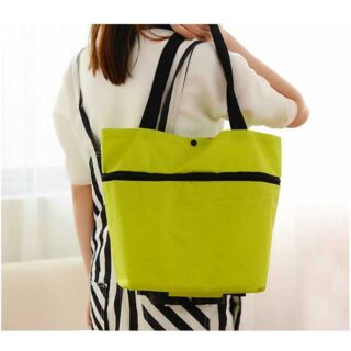 panier de courses à roulettes pliable en sac à main vert néon, porté par une femme de dos avec des cheveux bruns, un tee-shirt blanc et une jupe noire et blanche rayée