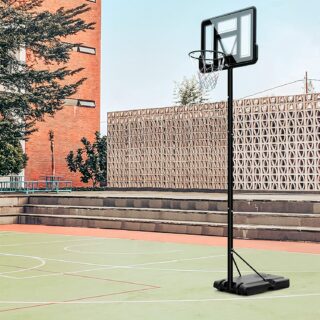 Dans une cour, on voir un panier de basket noir sur pied. Il est très grand, au moins trois mètres.