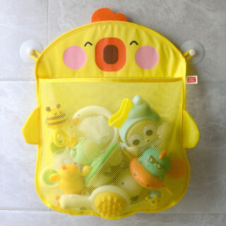 Suspendu au mur pat deux ventouses sur un carrelage gris, un panier rectangulaire jaune avec tête de poussin et filet avec des jouets de bébé colorés pour le bain à l'interieur.