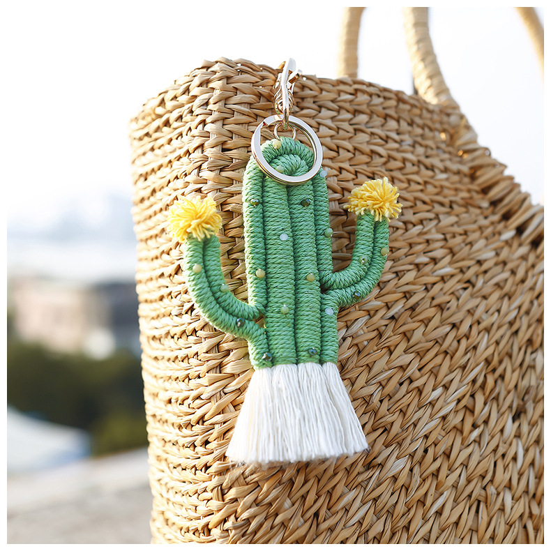 Sur un panier, on voit un porte-clé en forme de cactus, il est tissé en fils verts. Il a deux fleurs jaunes aux extrémités.