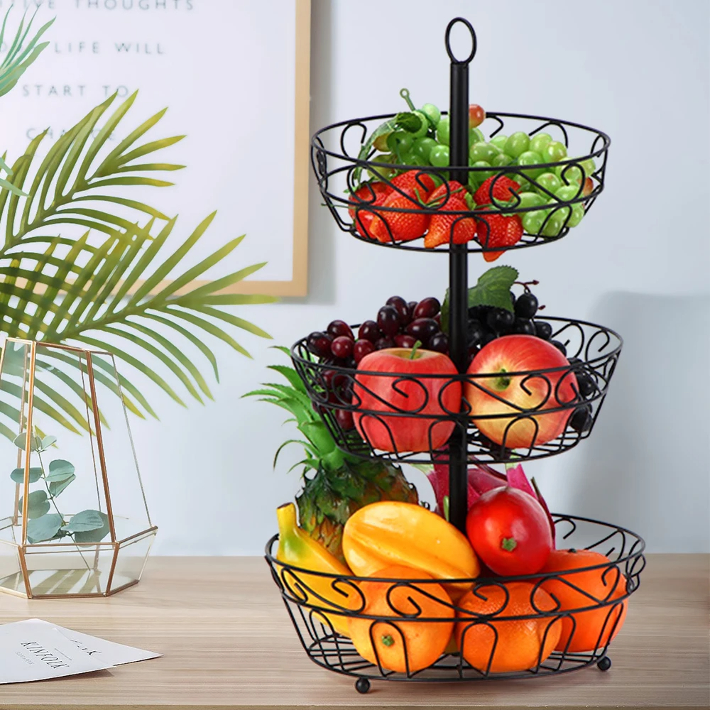Panier à fruits en métal à trois étages ici posé sur une table en bois.